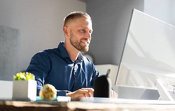 ein junger Mann im blauen Hemd sitzt vor seinem Computer