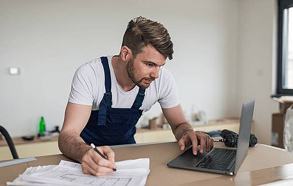 Ein Handwerker schreibt Notizen aus dem Computer ab in seinen Bauplan