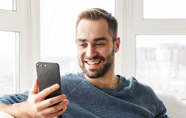 ein Mann sitzt auf einem Sofa und blickt auf sein Handy in seiner Hand