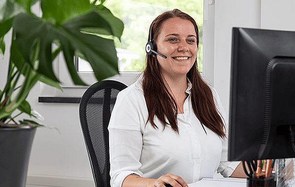 Frau mit Headset sitzt vor dem Bildschirm und lächelt freundlich 