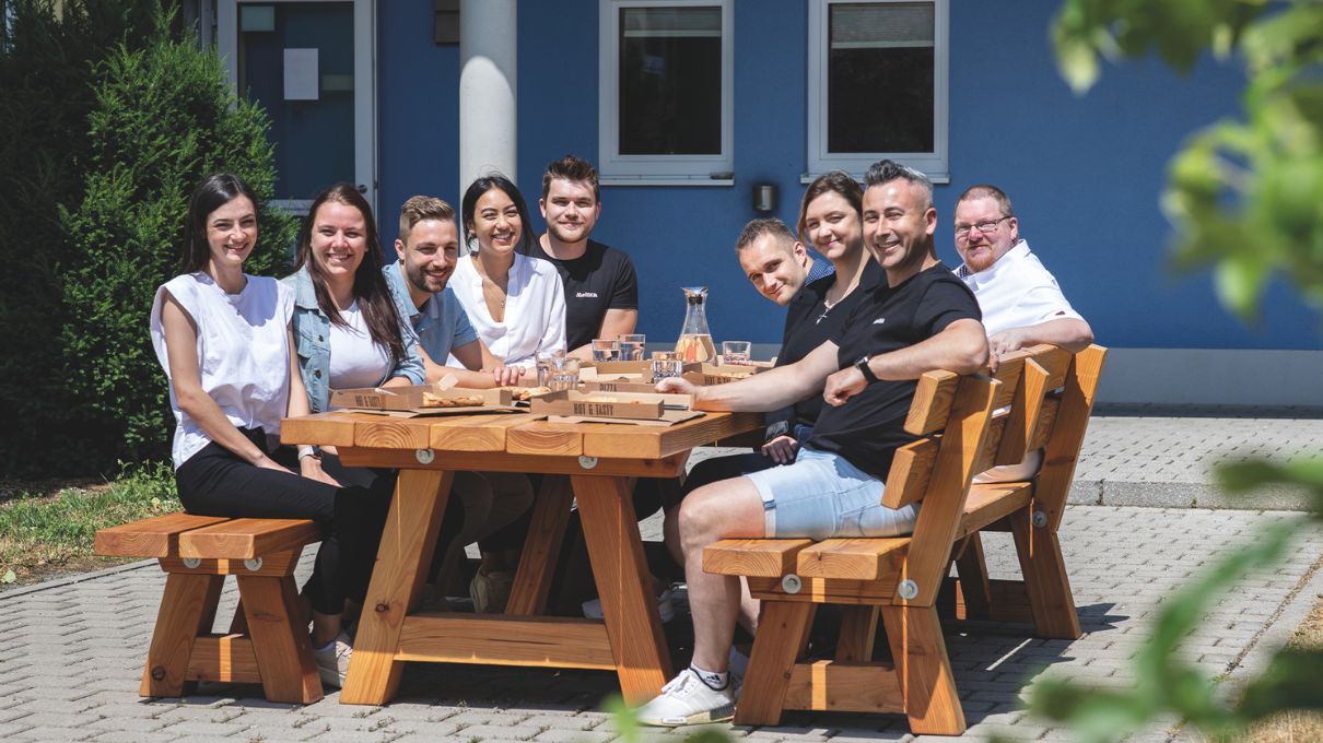 Einige Mitarbeiter der Firma Meltem sitzen an einem großen Tisch und essen Pizza