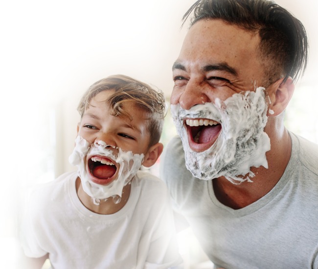 Vater und Sohn haben Rasierschaum im Gesicht und lachen vor dem Spiegel